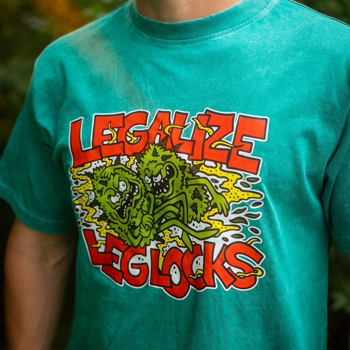 Close-up of the Legalize Leg Locks '25 graphic on a teal mineral wash t-shirt. Features original artwork by Joe Tamponi for Rubber Bones.