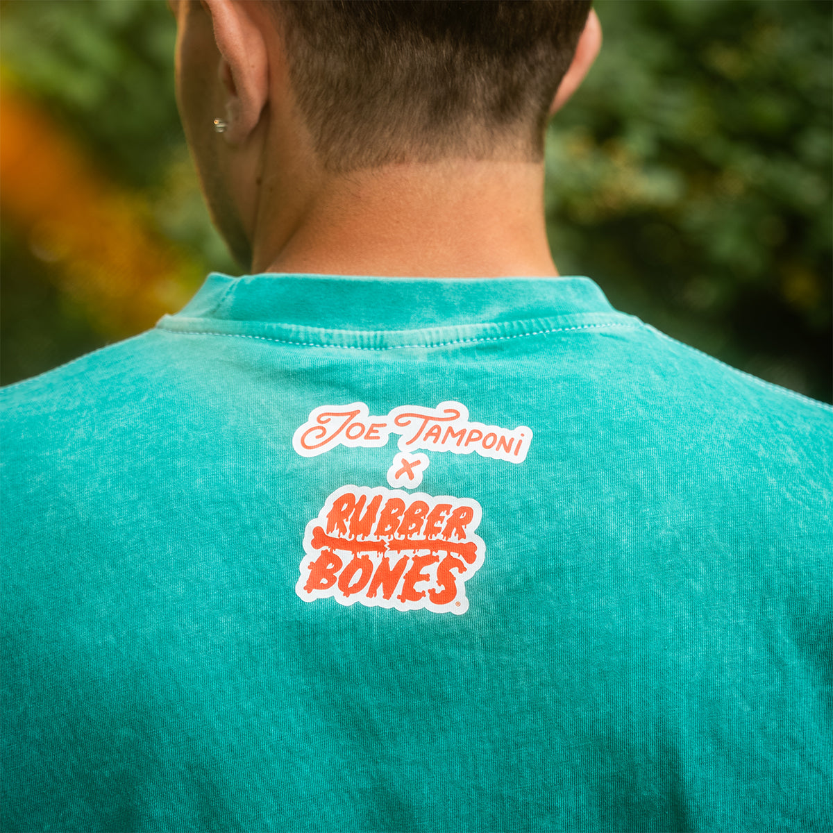 Back neck detail of the Rubber Bones x Joe Tamponi collaboration tee, printed on teal mineral wash cotton. Legalize Leg Locks limited edition.