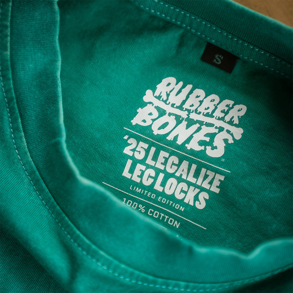 Interior label print showing Rubber Bones Legalize Leg Locks '25 limited edition details inside teal mineral wash t-shirt.