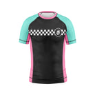 Youth-sized short-sleeve rash guard with a black front panel, teal sleeves, and pink side panels. A white checkerboard stripe spans the chest with a Rubber Bones skull logo on the left side.
