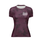 Rubber Bones 'Natural Grappler' Women's BJJ Rash Guard – Front View. Maroon short-sleeve rash guard with a subtle black tie-dye pattern. A small white chest logo displays 'The Natural Grappler' and 'Rubber Bones' in a hand-drawn, artistic style.