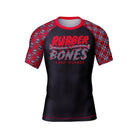 Black rash guard with red skull-patterned sleeves. The chest features "Rubber Bones" in bold, dripping red and gray letters, with "Rash Guards" written below in a distressed-style font.