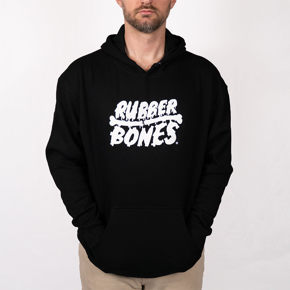 Man wearing black Rubber Bones logo hoodie with white skull graphic centered on chest, showing full product fit, kangaroo pocket, and relaxed silhouette.