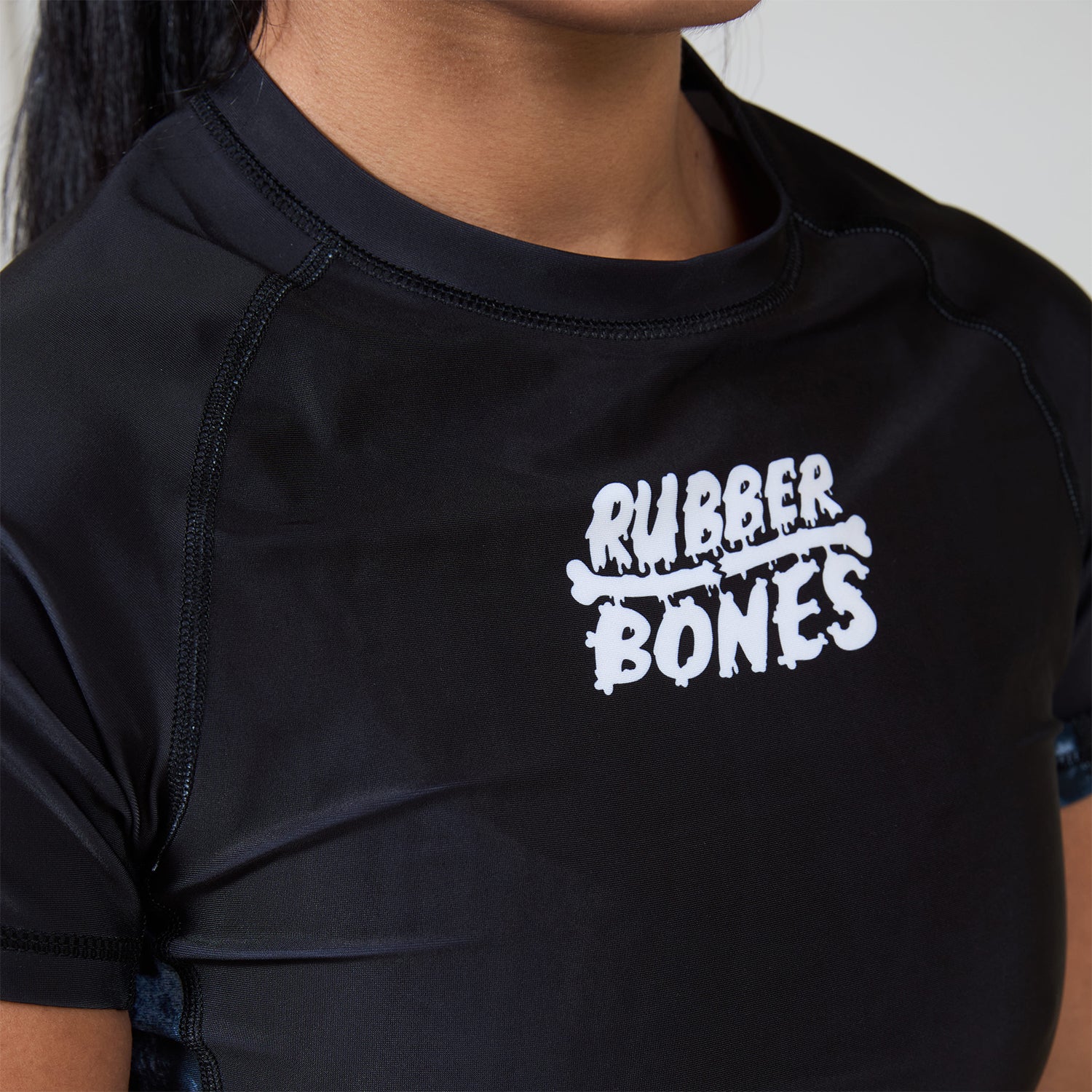 Close-up of white Rubber Bones logo printed on the chest of the Women’s Ash BJJ Rash Guard.