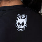 Close-up of white melting skull Rubber Bones logo printed on the back neckline of the Women’s Ash BJJ Rash Guard.
