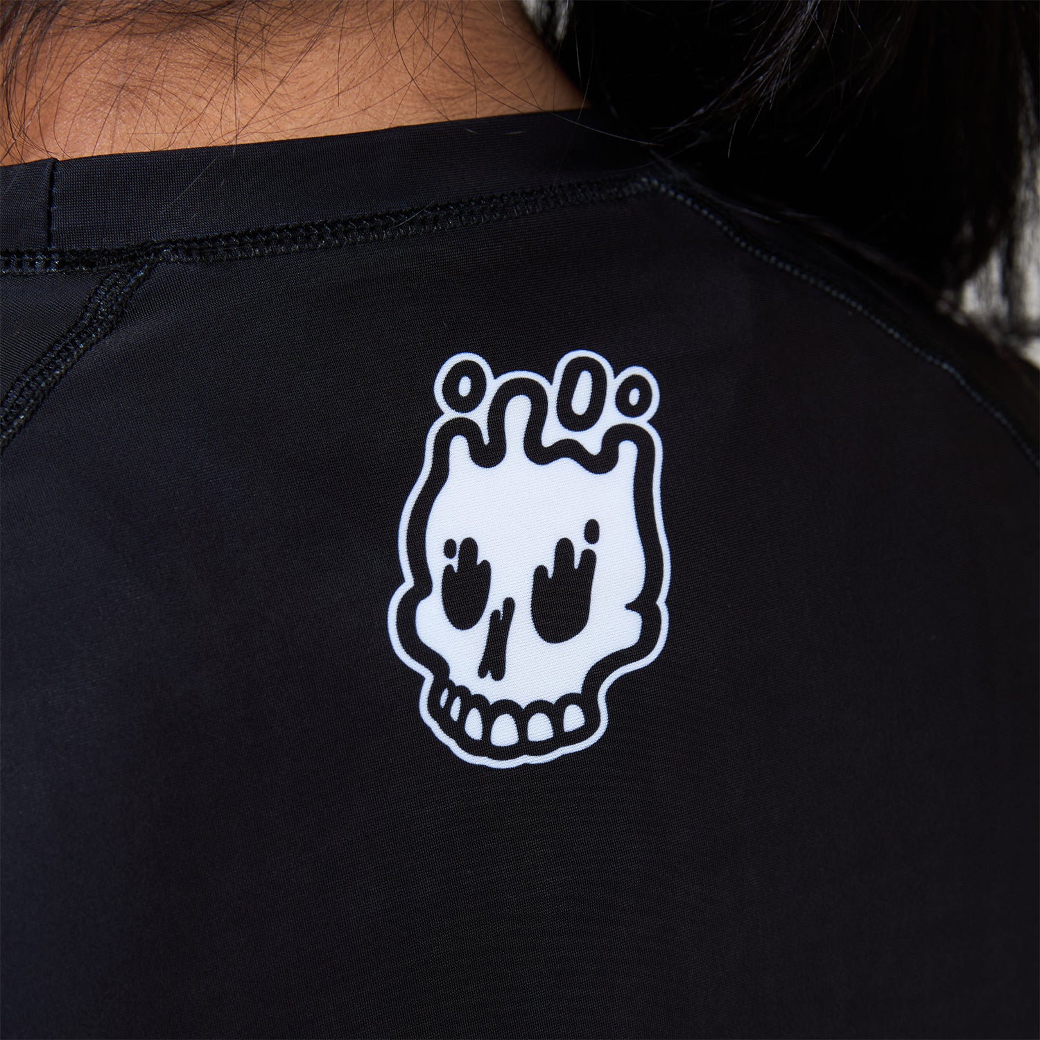 Close-up of white melting skull Rubber Bones logo printed on the back neckline of the Women’s Ash BJJ Rash Guard.