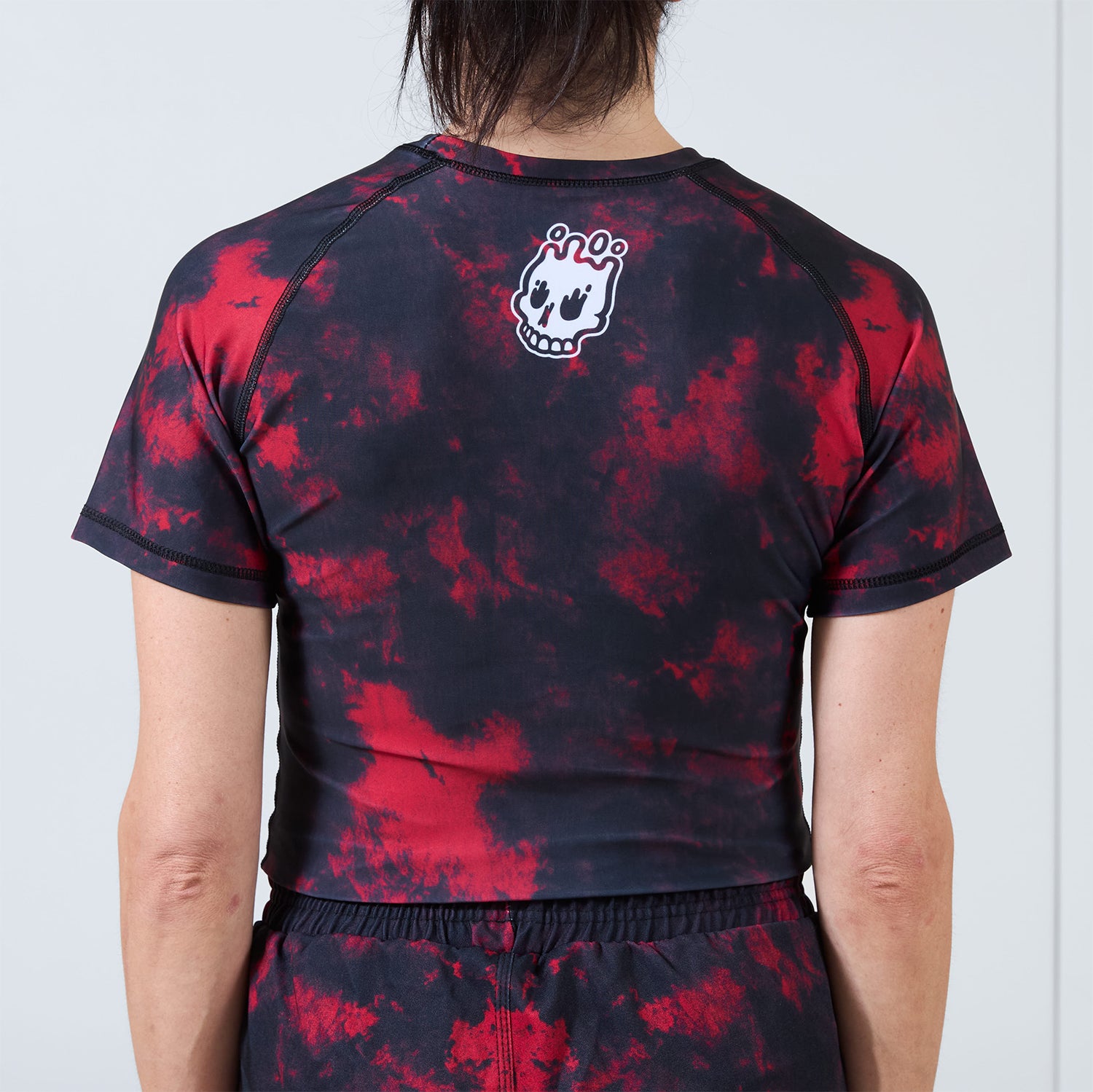 Back view of the Women’s Ember BJJ Rash Guard showing red and black pattern with white skull logo near neckline.