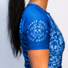 Side View: Side close-up of a blue ranked Brazilian Jiu-Jitsu rash guard. Dripping skull logo with "Rubber Bones Rash Guards" text on the sleeve. High-quality sublimated print with reinforced seams.