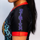 Side view of the Rubber Bones Tora Oni women's rash guard sleeve – Japanese lettering in purple outlined in teal on a black background with red stitching.