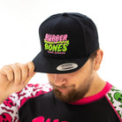 On-body shot of male model tipping OG Snapback Hat forward, highlighting bold Rubber Bones design.